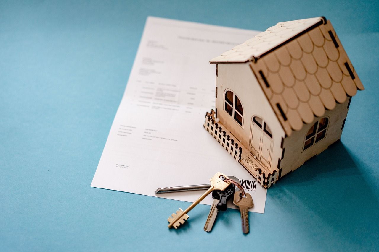 Wooden house model, keys, and document on a blue surface, representing a real estate transaction.