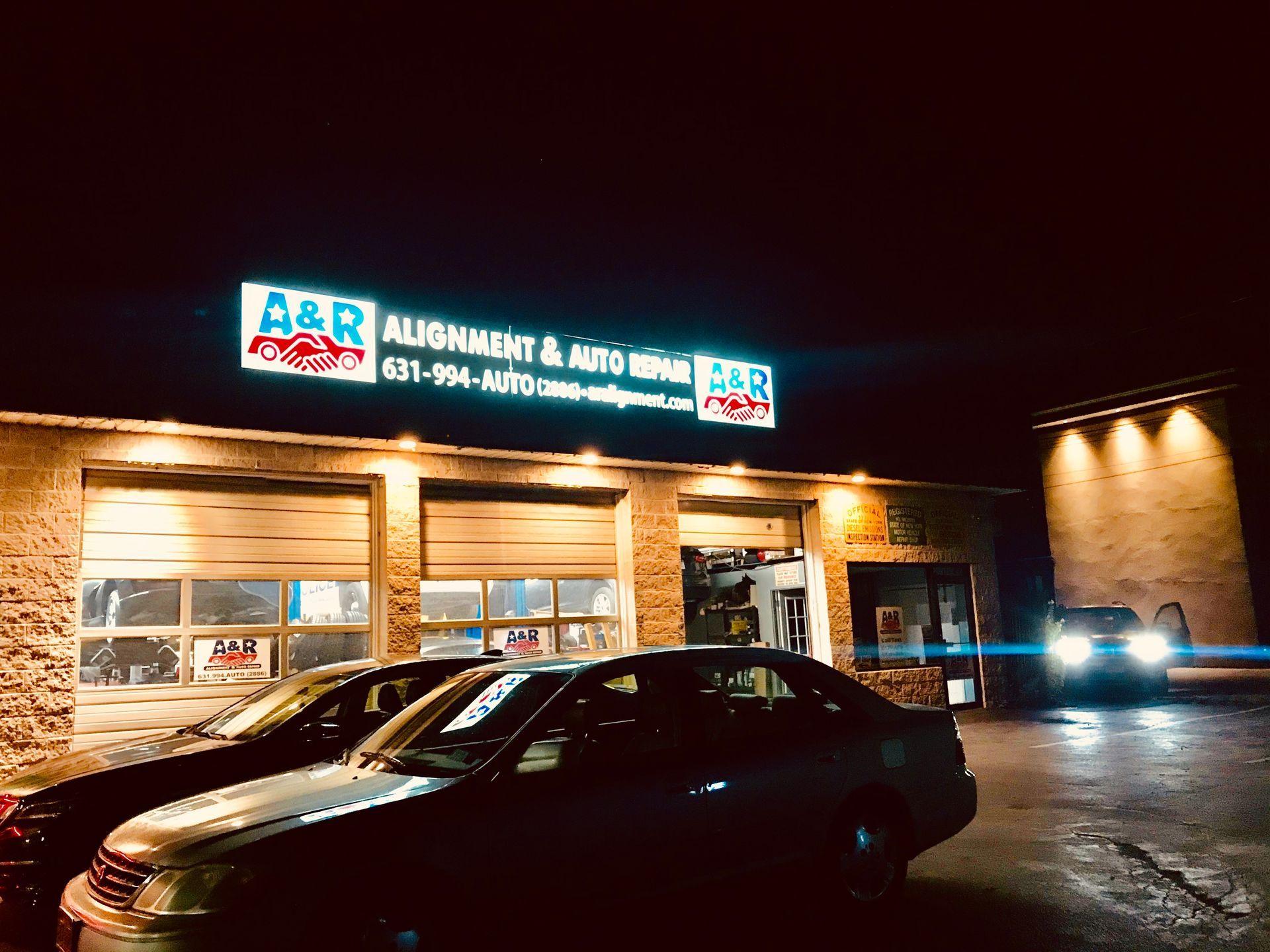 A&R Alignment & Auto Repair shop at night, illuminated sign above garage doors. Cars parked outside. | A & R Auto Repair