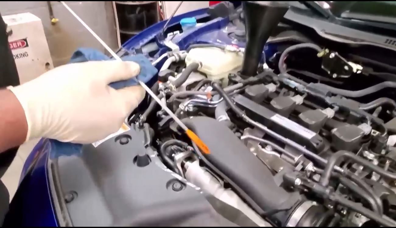 A mechanic checking engine oil levels in a blue car with a dipstick and funnel. | A & R Auto Repair