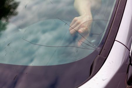 Une personne touche le pare-brise fissuré d'une voiture.