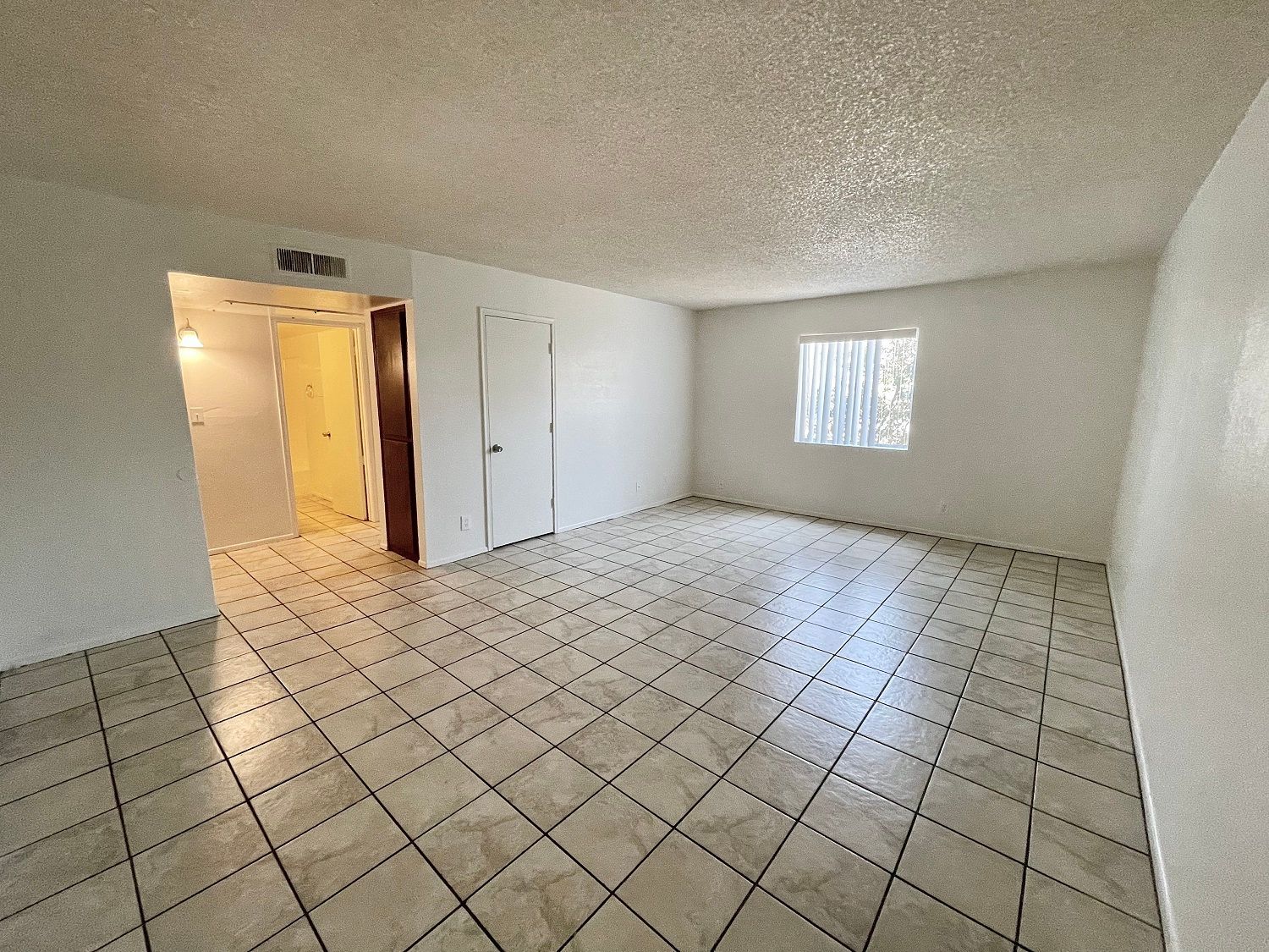 Empty room with white walls, tiled floor, and a window; doorway leads to another room.