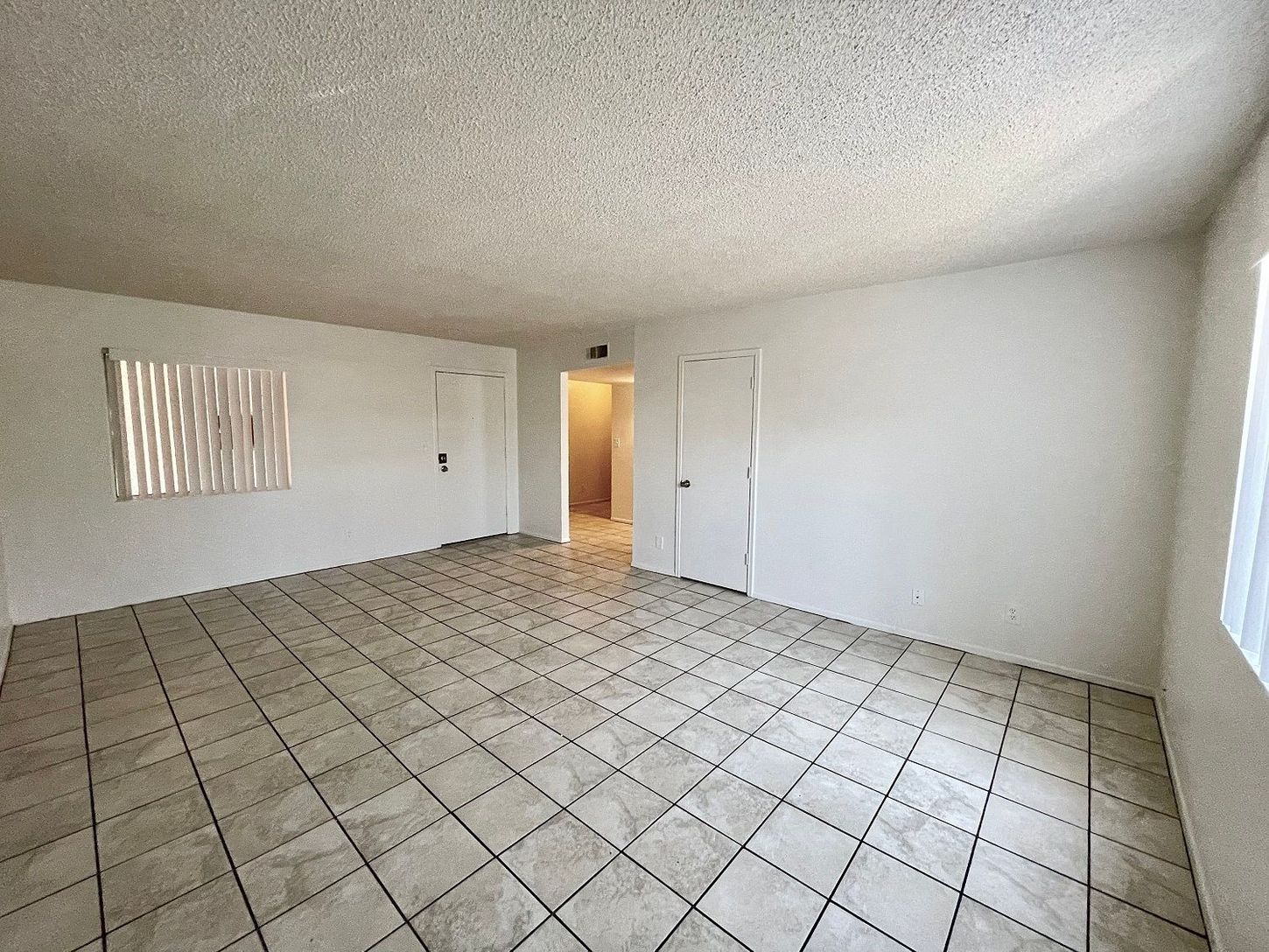 Empty room with tiled floor, white walls, two doors, and a window with blinds.