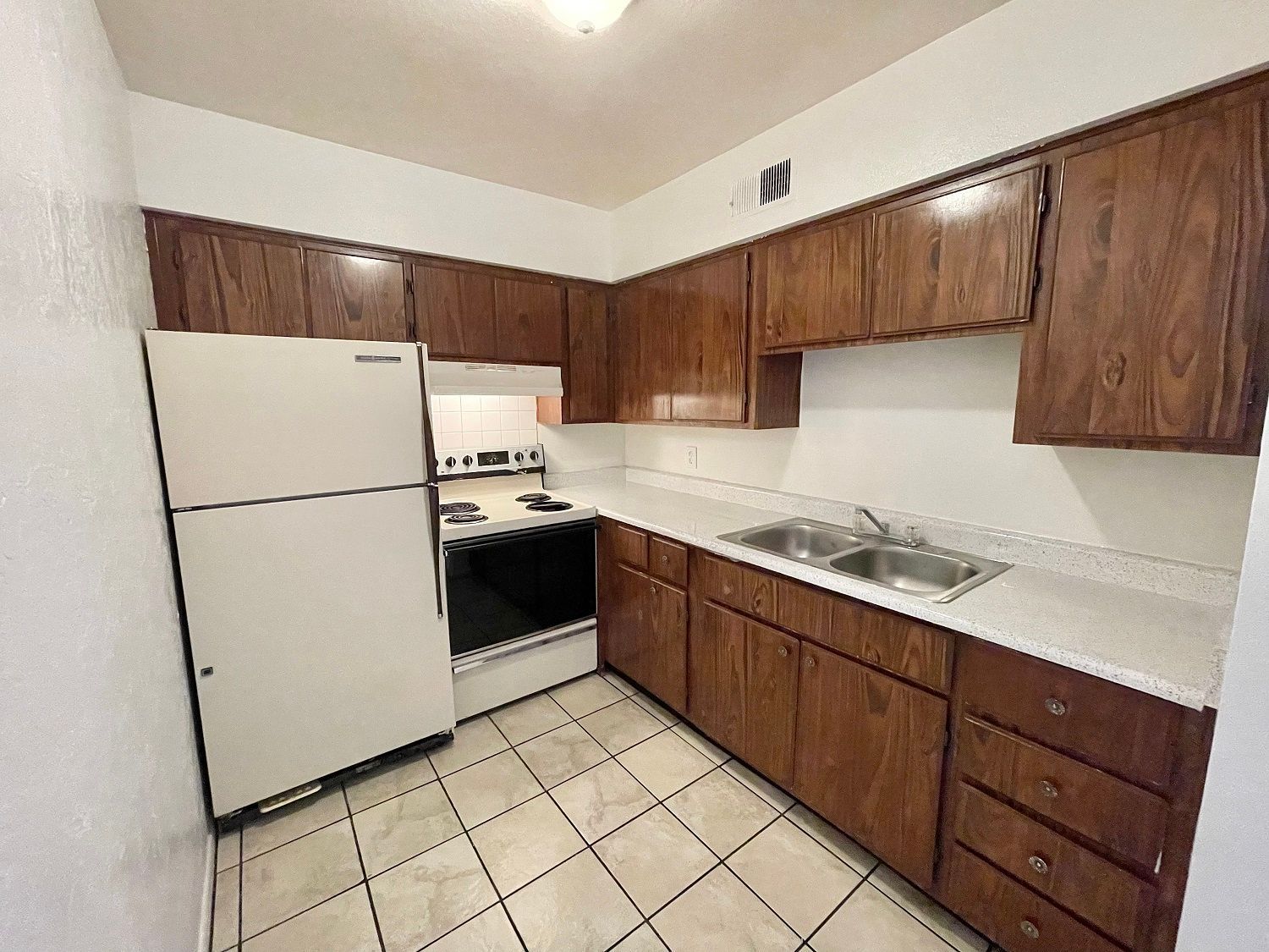 Kitchen with brown cabinets, white refrigerator and stove, and tiled floor.