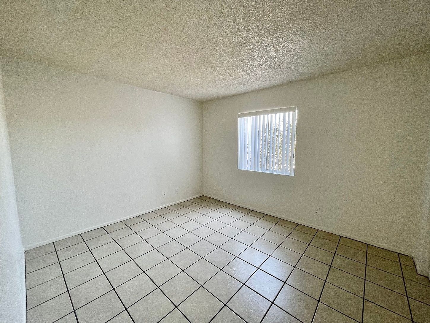 Empty room with white walls, tiled floor, and a window with blinds.