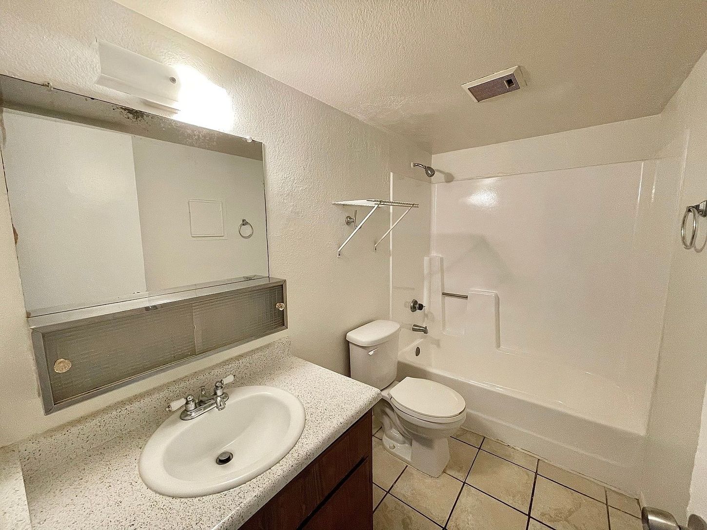 Bathroom with a white tub and toilet, sink, and mirror. White walls and tan tiled floor.