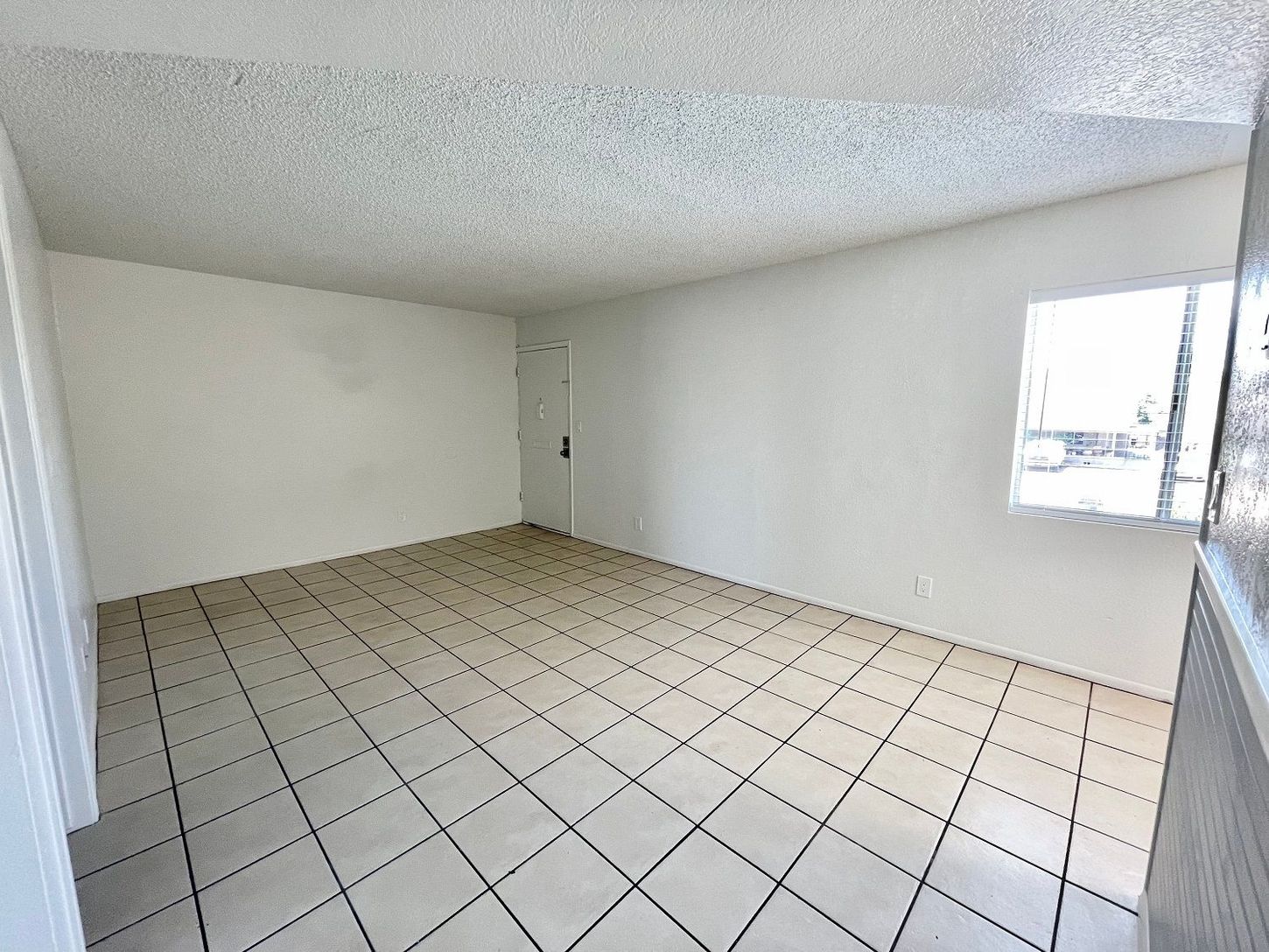 Empty room with white walls, tiled floor, and a window; door in the back.