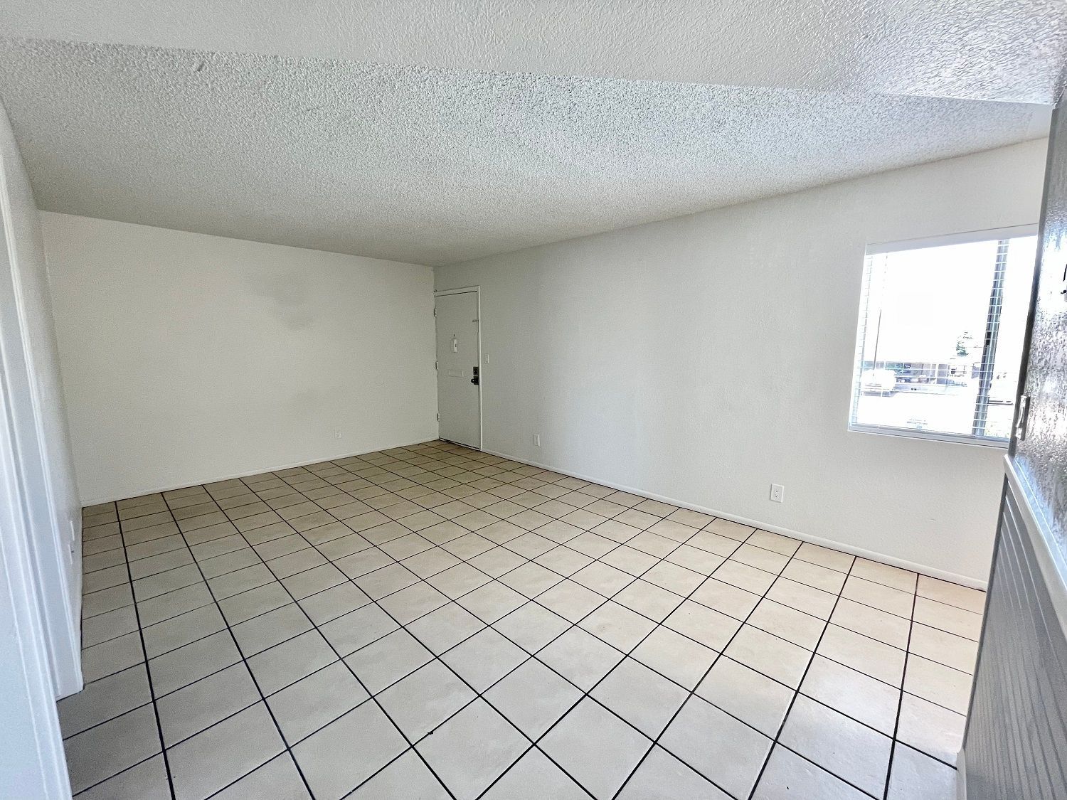 Empty room with white walls, tiled floor, and a window; door in the back.