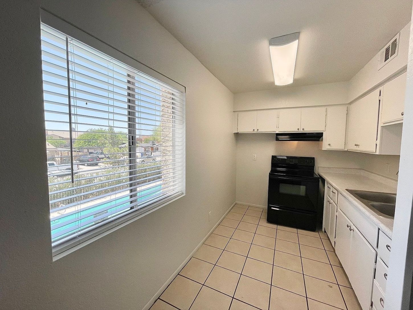 Kitchen with white cabinets, black stove, window with blinds, and tile floor.