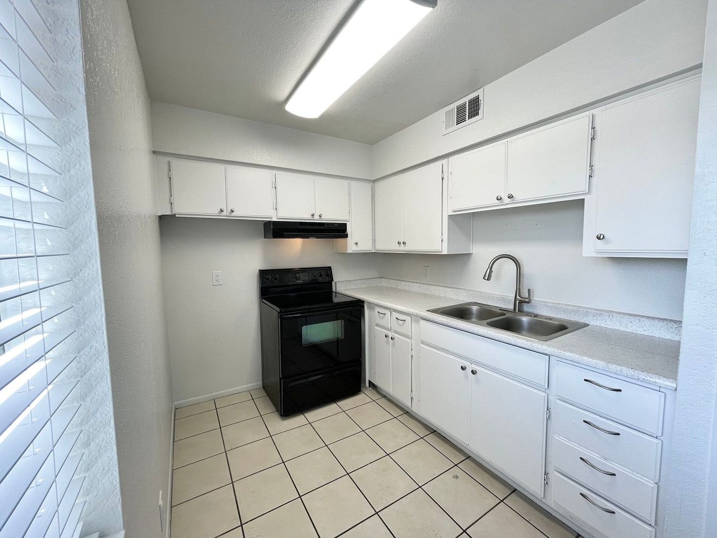 Kitchen with white cabinets, light countertops, black oven, and tiled floor.