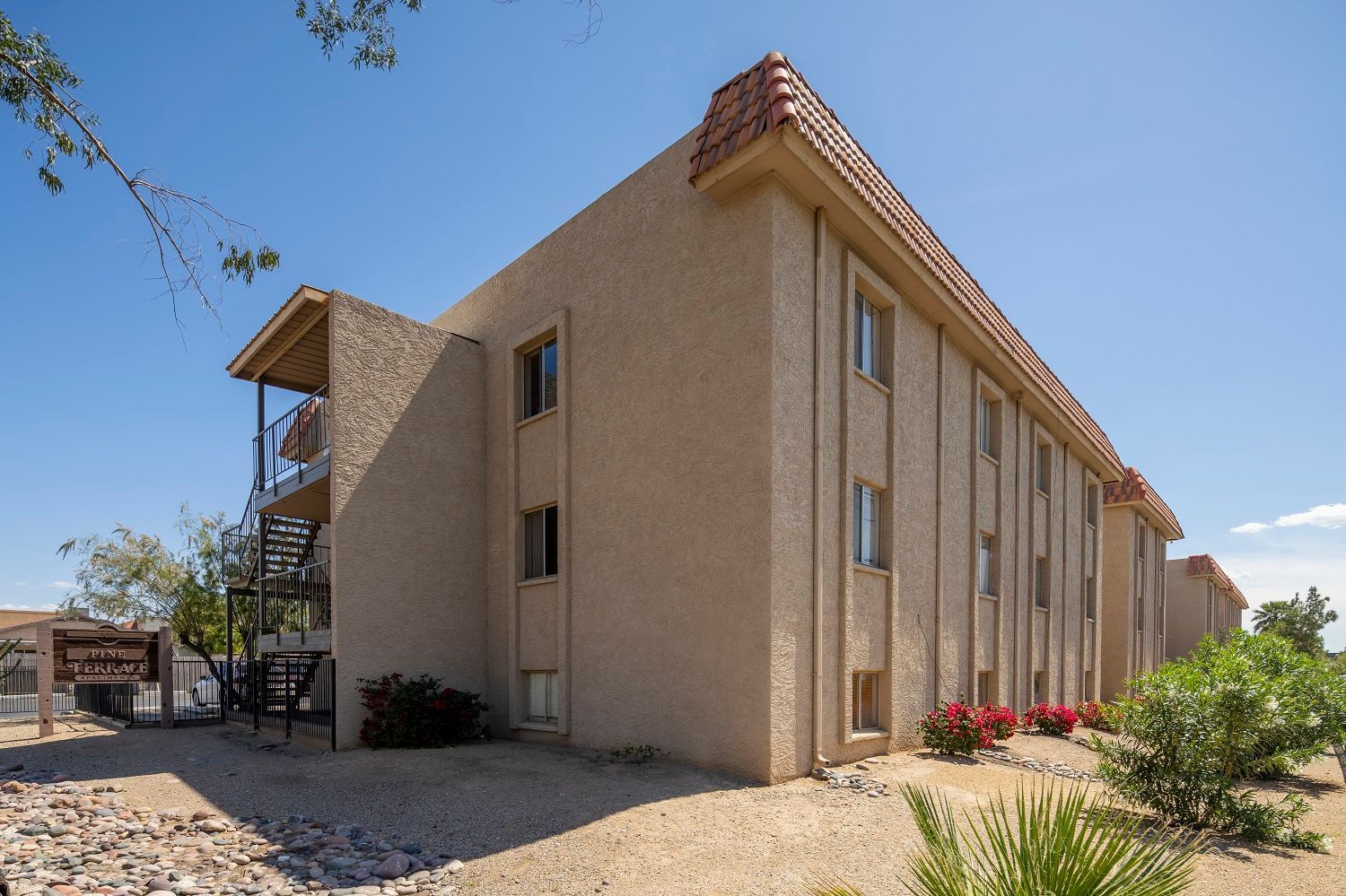 Tan stucco apartment building with balconies, under a blue sky, with desert landscaping.