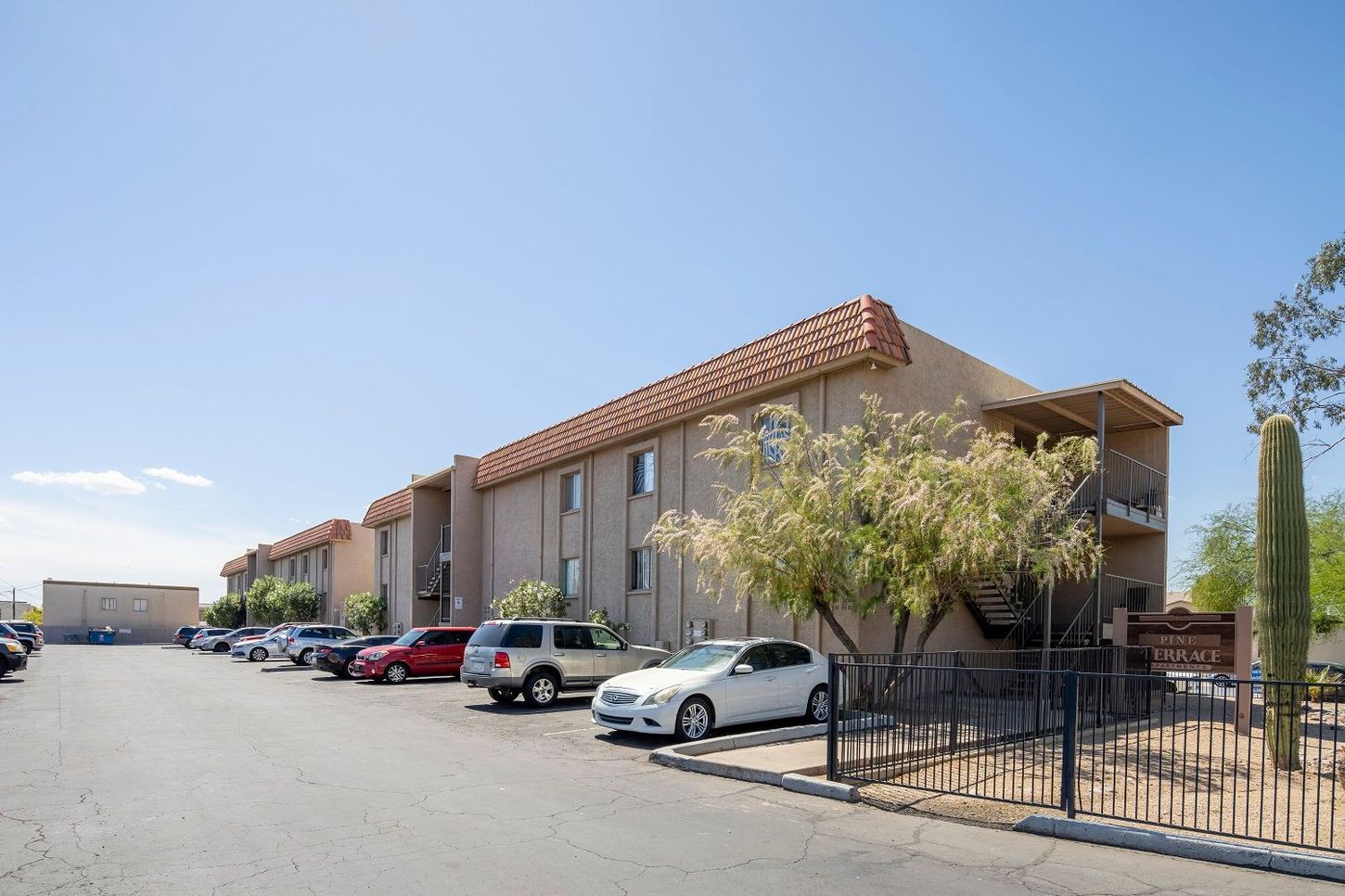 Apartment building with parked cars, a tan exterior, and a blue sky.