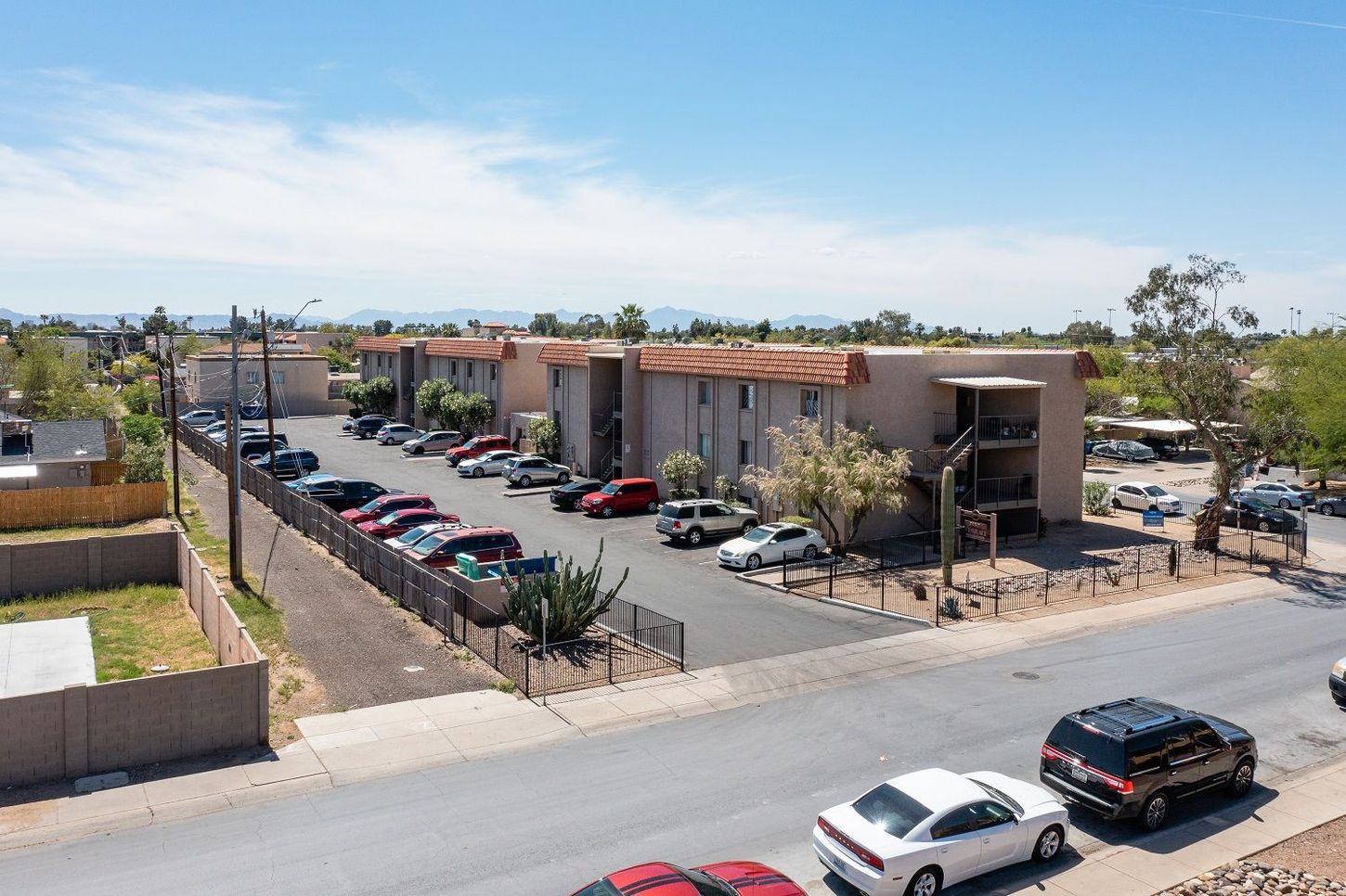 Apartment complex with parked cars, tan buildings, and a blue sky.