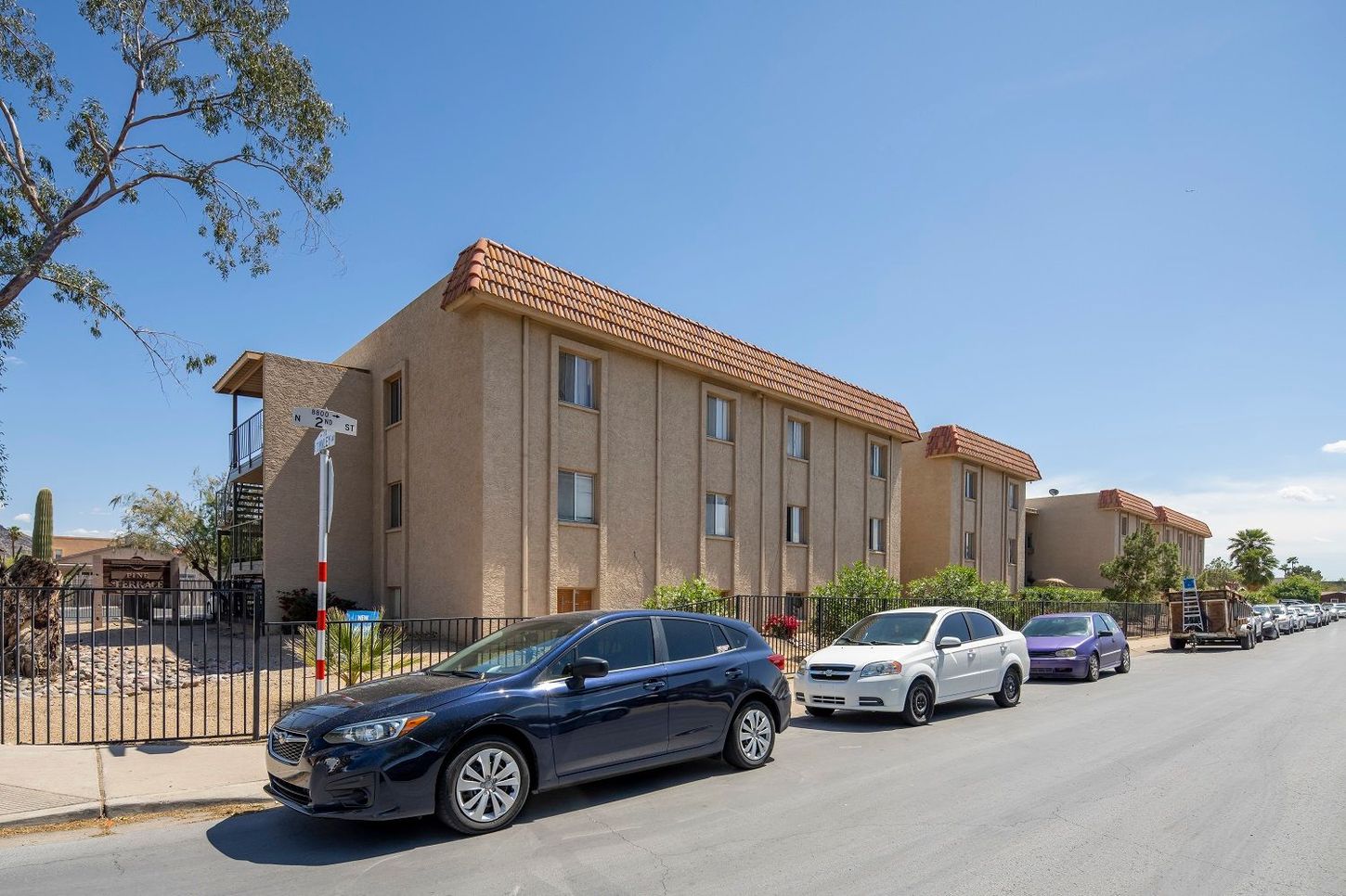 Apartment building with cars parked on the street on a sunny day.