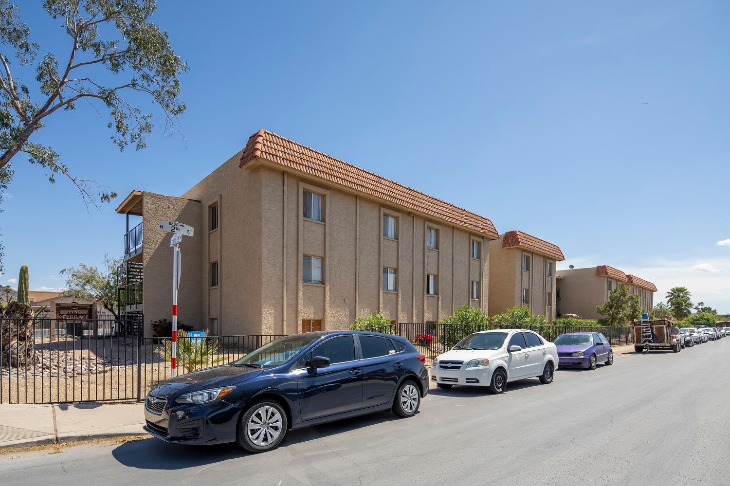 Apartment building with cars parked on the street on a sunny day.