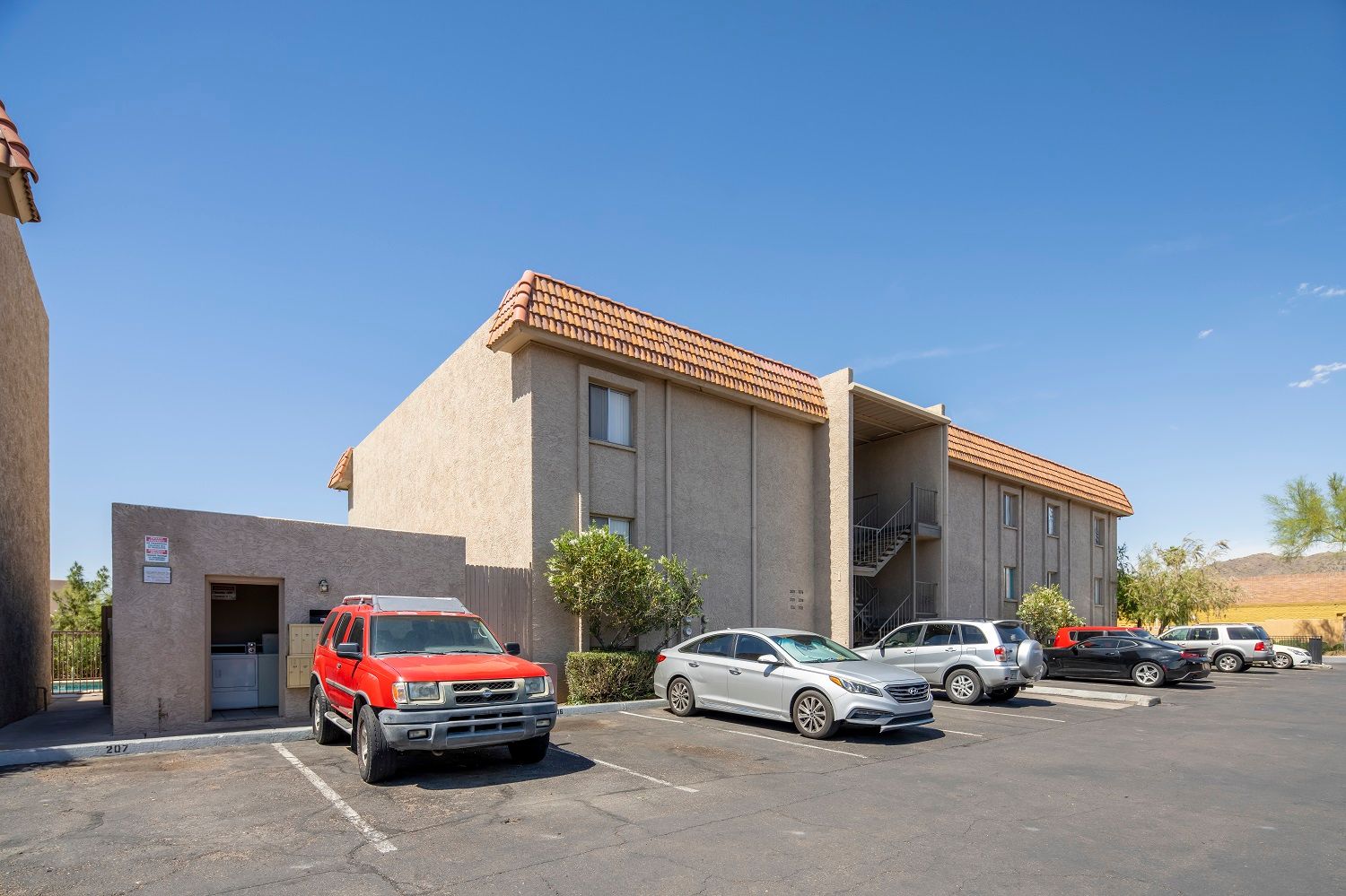 Apartment building with cars parked out front on a sunny day. Beige stucco exterior.