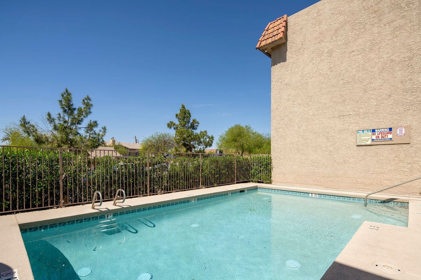 Small outdoor swimming pool next to a beige building under a blue sky.
