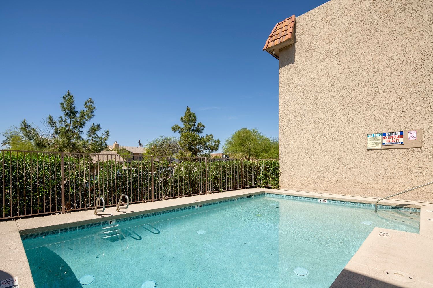 Small outdoor swimming pool next to a beige building under a blue sky.
