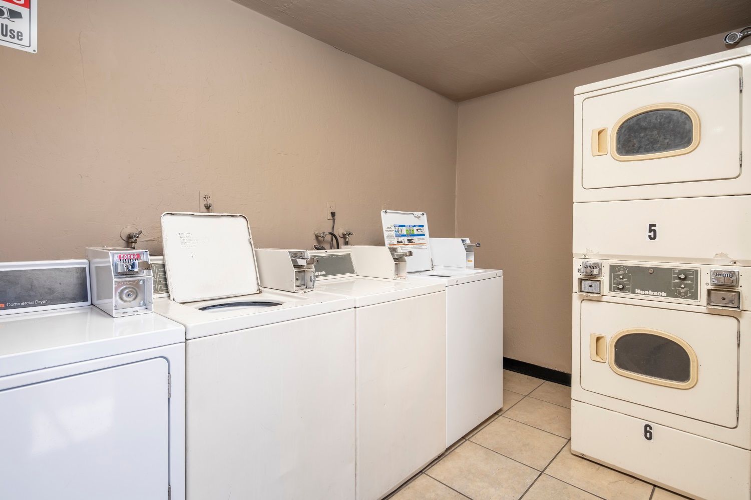 Laundry room with several white washing machines and a stacked dryer.