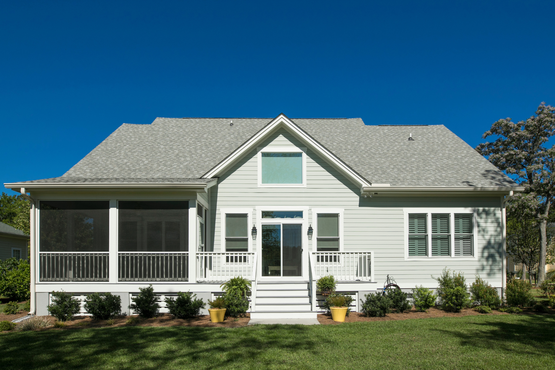 The back of a white house with a screened in porch.