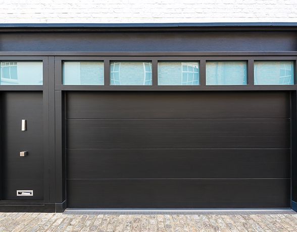 a black garage door with a brick driveway in front of it