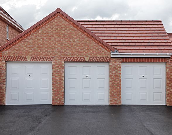 a brick house with three white garage doors and a red roof