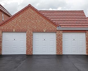 a red brick house with three white garage doors and a red tile roof .