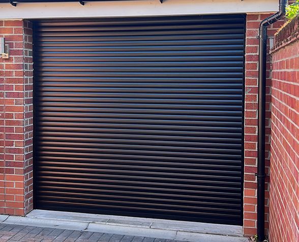 a black garage door is sitting next to a brick wall .