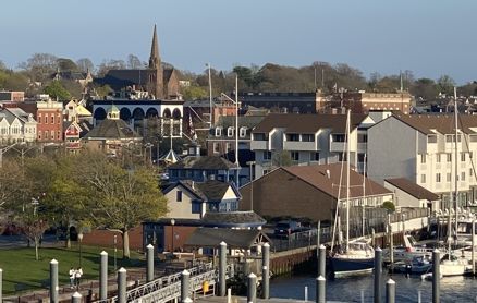 A high-angle view of a resort pool area with blue umbrellas, palm trees, and a sandy beach with crowds by the ocean.