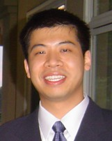 A person wearing a suit and tie smiles while posing for a headshot in front of a window.