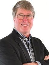 A person wearing glasses and a striped shirt under a black blazer, smiling with arms crossed against a white background.