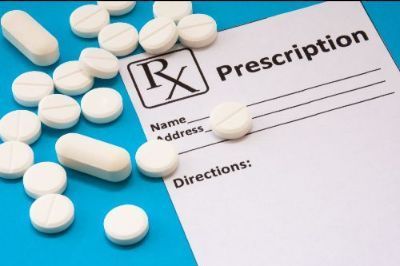 A blank prescription pad with the Rx symbol sits on a bright blue surface surrounded by many white pills.