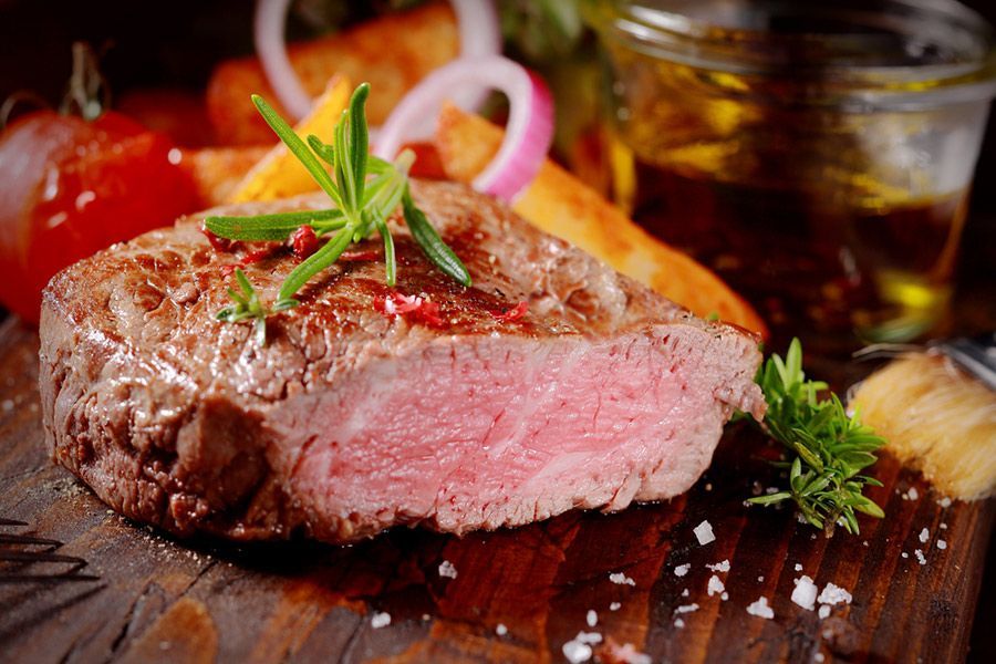 A Close Up of a Steak on a Wooden Cutting Board With Vegetables — LZH Butchers in Bungalow, QLD
