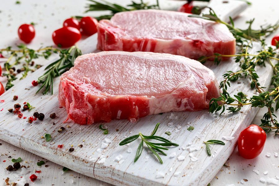 Two Raw Pork Chops Are Sitting on a White Cutting Board— LZH Butchers in Bungalow, QLD