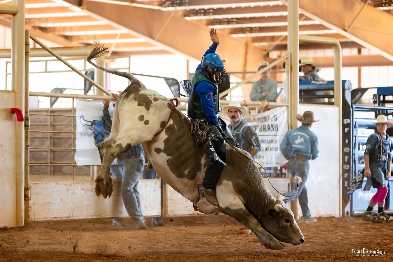 Bull rider on a bucking bull at an arena. Rider in blue jacket, bull in mid-air.