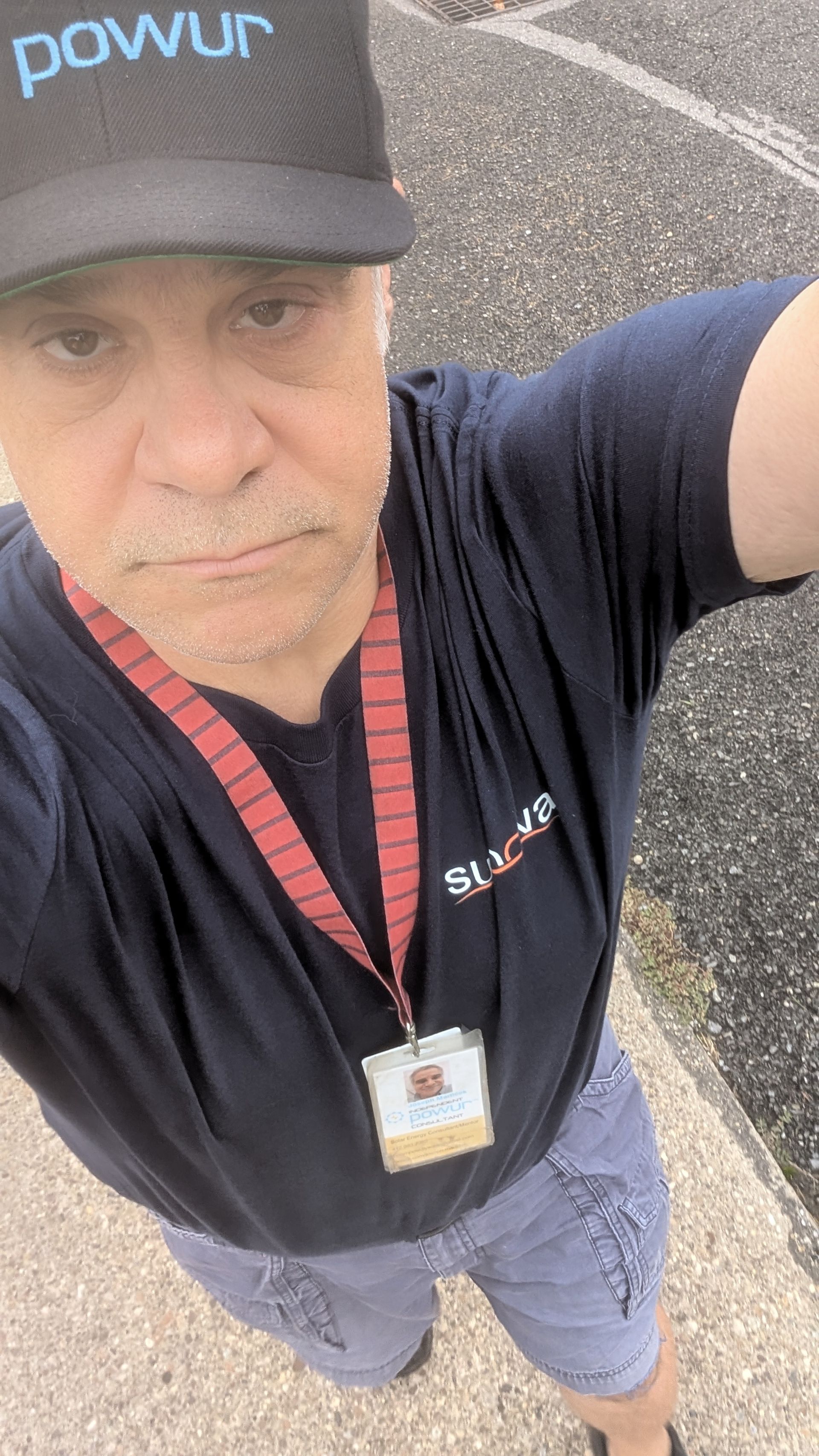 A man wearing a black hat and a lanyard is taking a selfie.