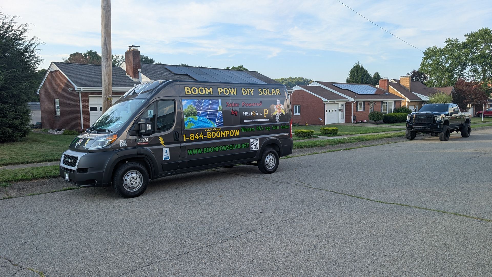 A food truck is parked on the side of the road in front of a brick house.