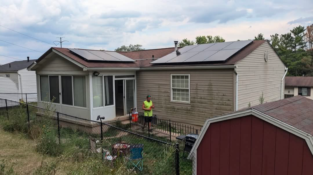 Backyard view of a house with solar panels on the roof, a worker in safety vest, and a red shed.