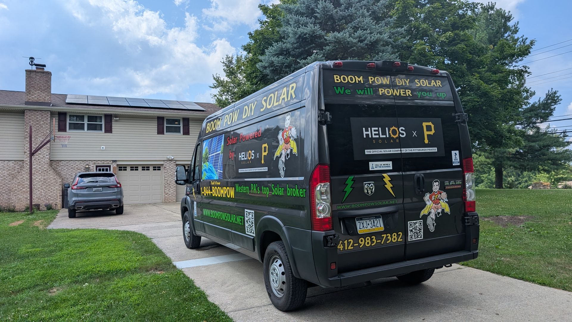 A black van with solar panel advertising parked in a driveway in front of a house with solar panels on the roof.
