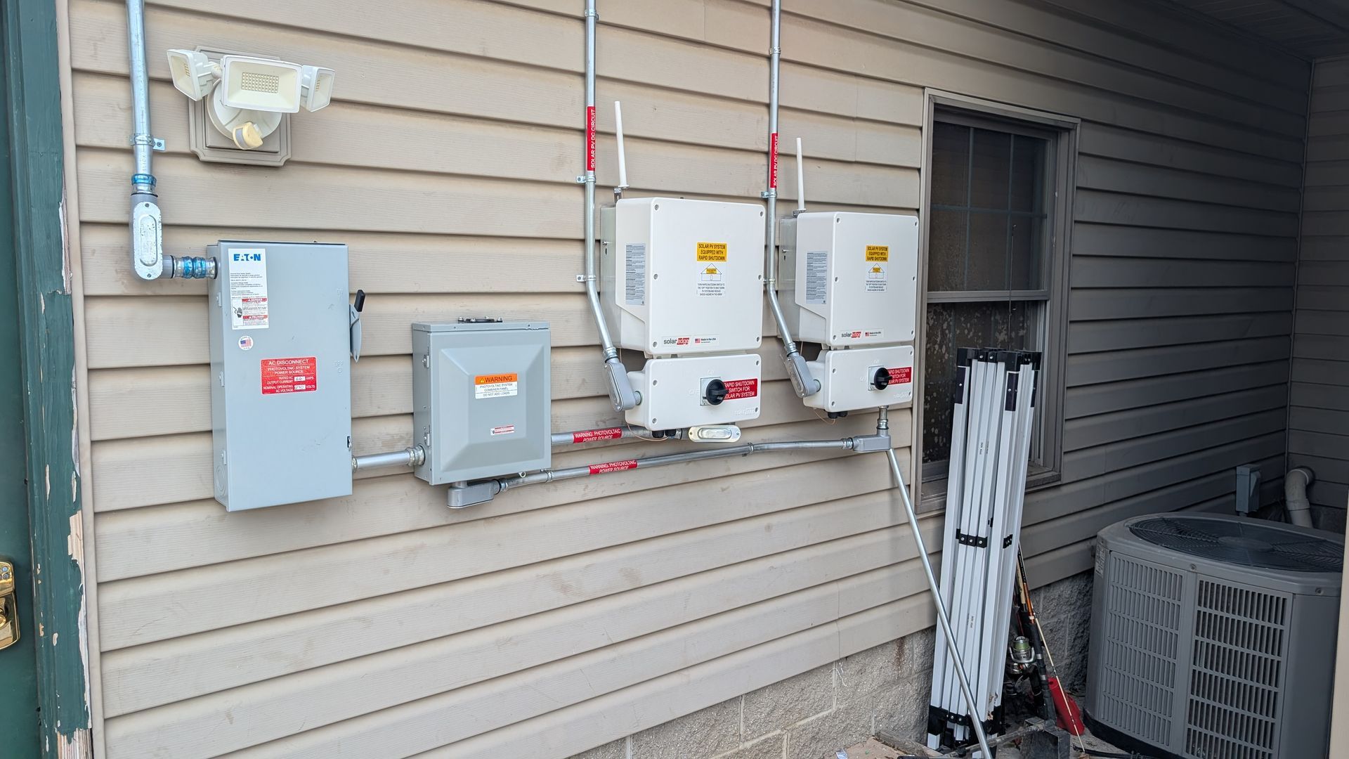 Solar panel inverters and electrical components are mounted on a beige siding wall.