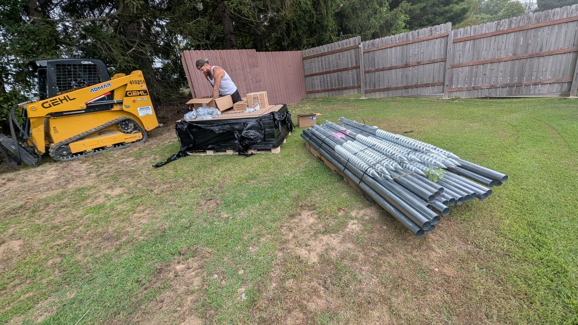 Yellow skid steer, person, fence, and metal poles on green grass.