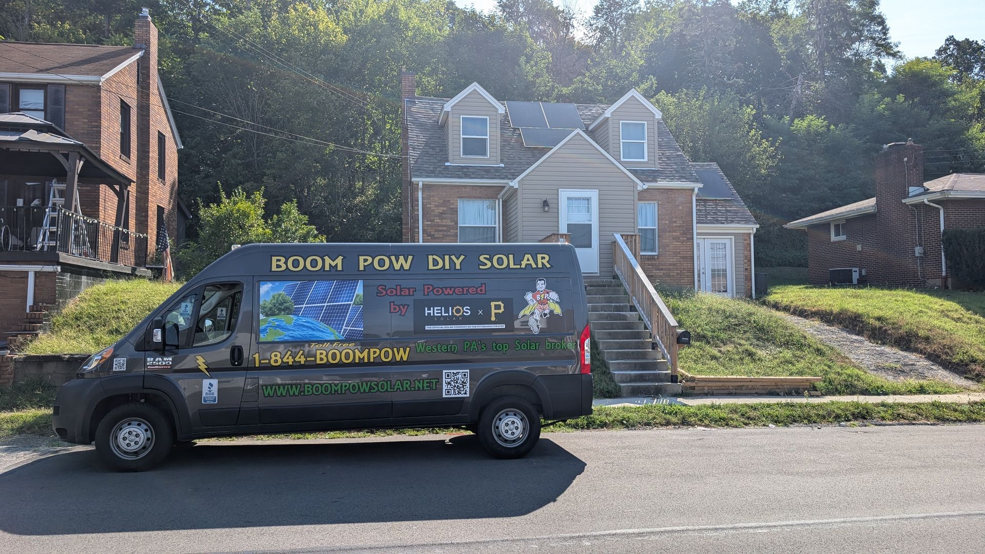A solar panel van parked in front of a house; sunny day with green foliage.