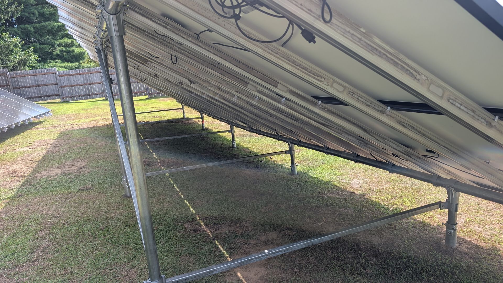 Underside view of solar panels on a metal frame in a grassy field.
