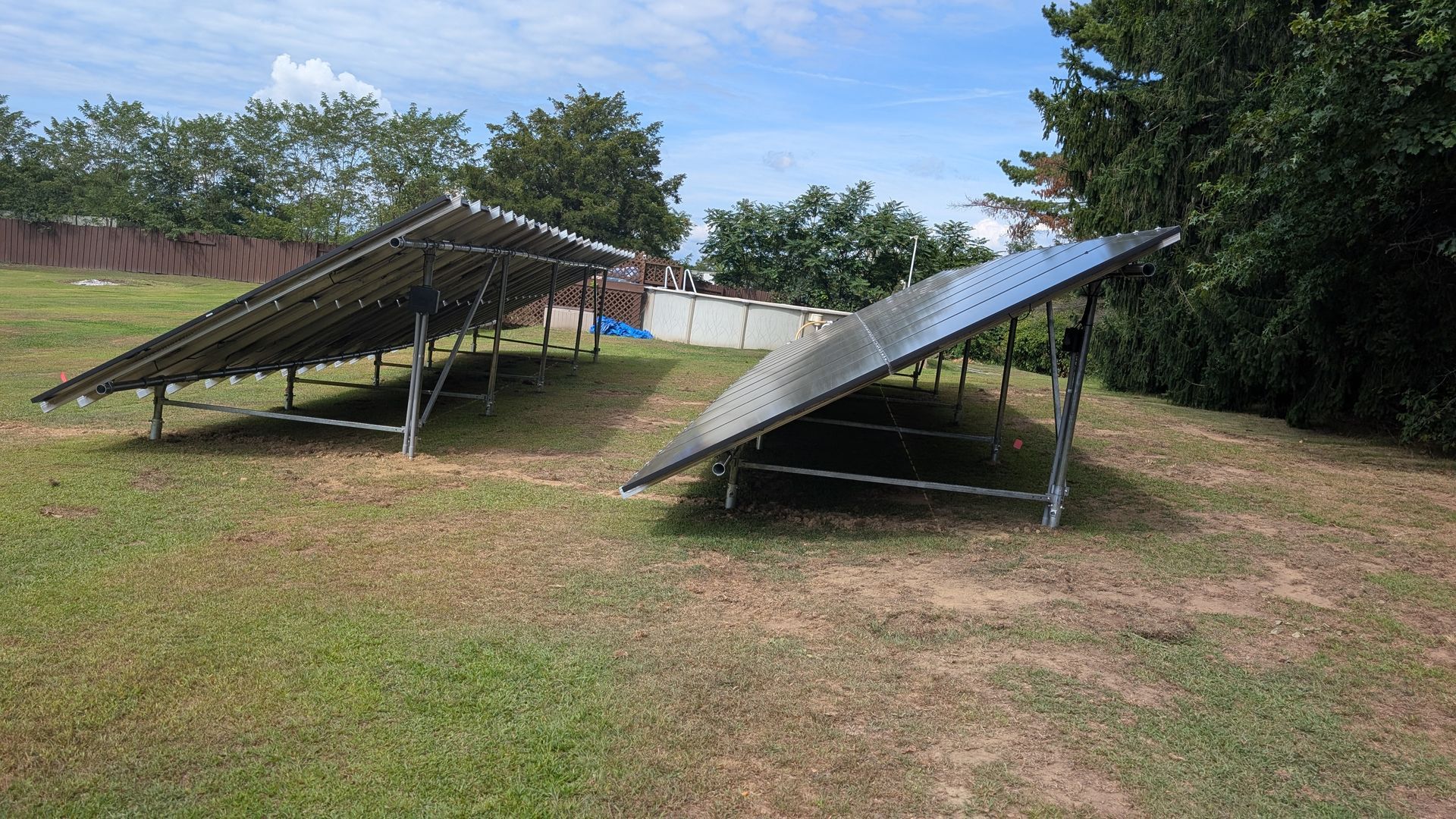 Two angled solar panel arrays in a grassy yard with trees in the background.