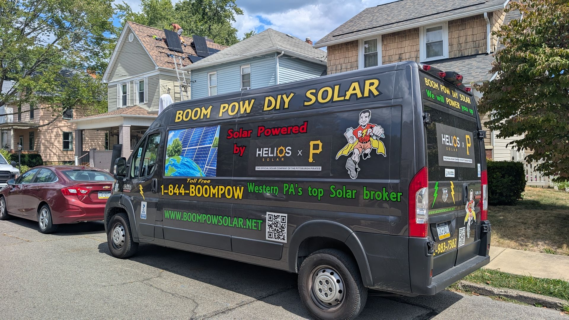 Black van with solar panel ad parked on a street; houses in the background.