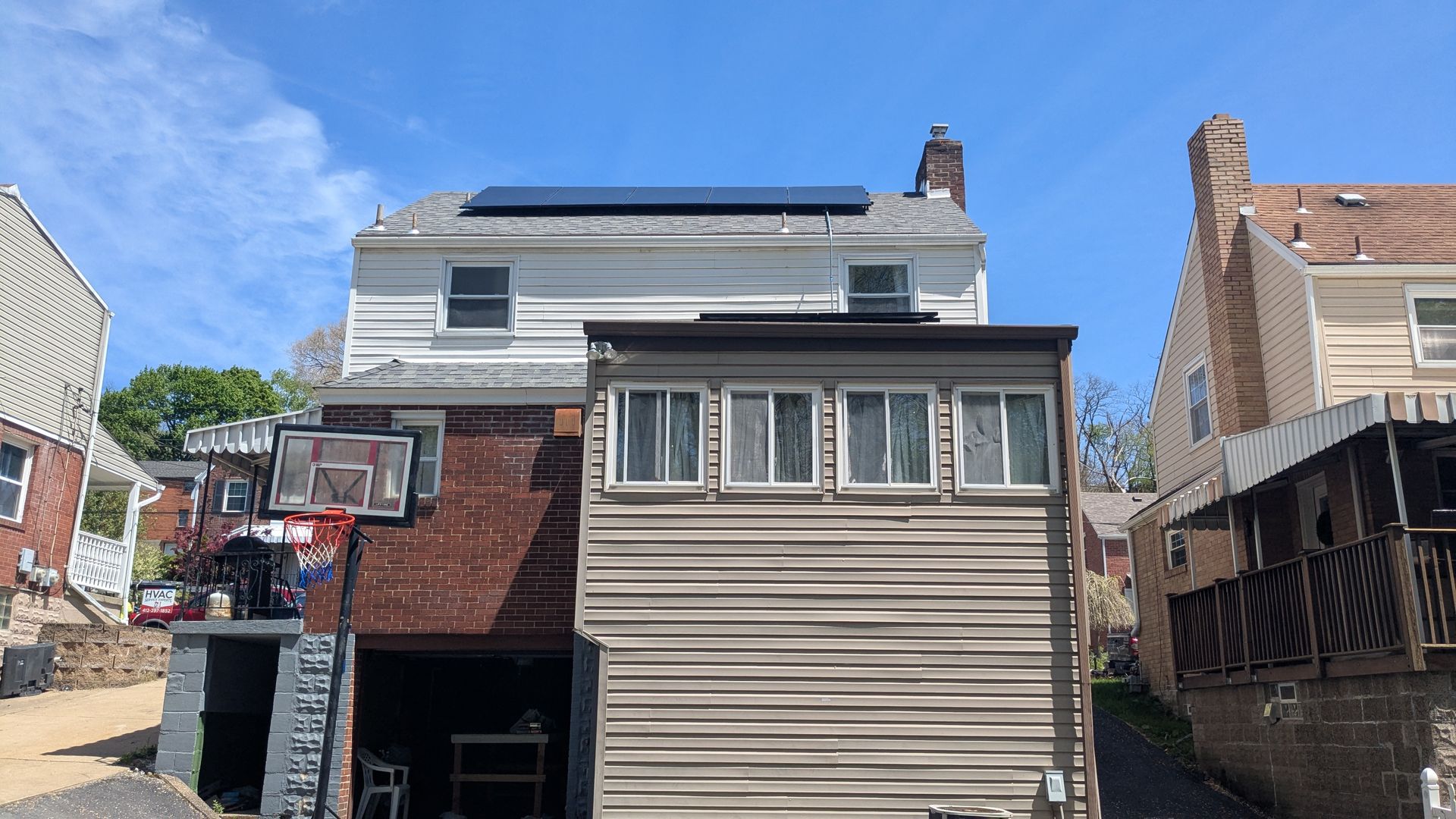 Back view of a two-story house with solar panels, a basketball hoop, and a garage, with a clear blue sky.