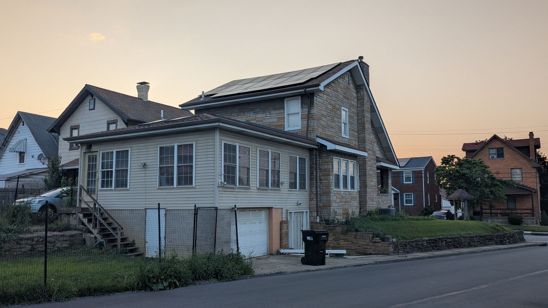 A house with solar panels on the roof is sitting on the side of the road.