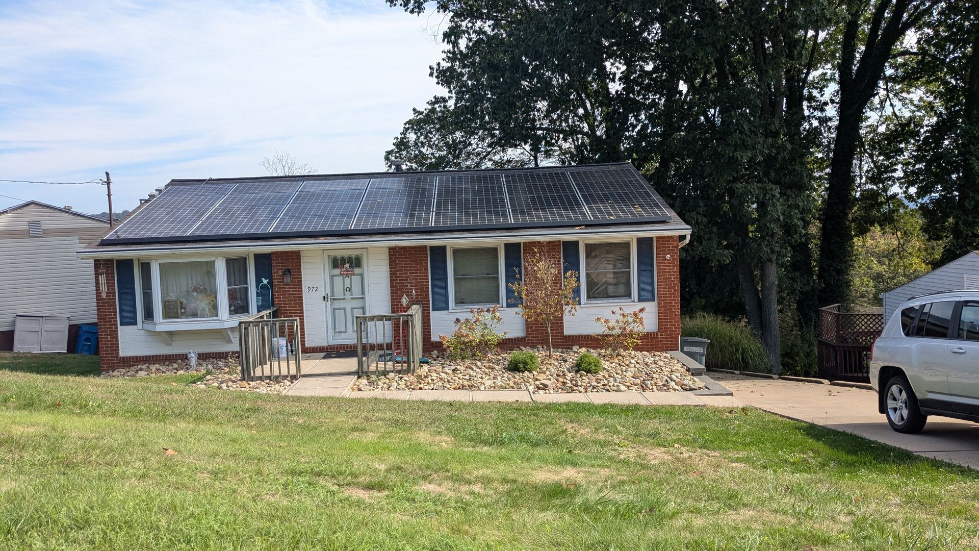 A small, brick house with a dark roof, surrounded by a yard and a driveway with a parked car.