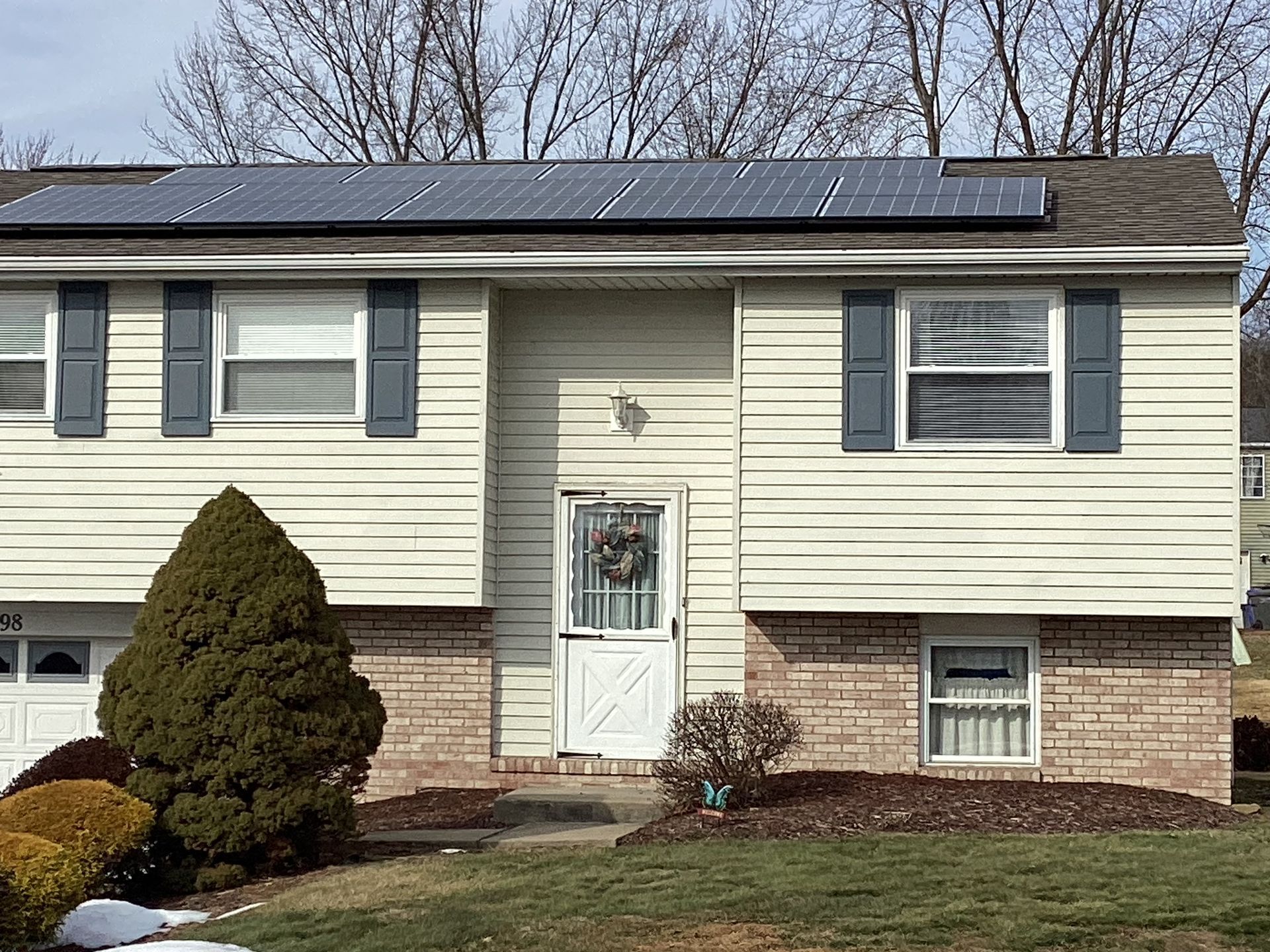 House with solar panels on roof, shutters, brick facade, and front lawn.