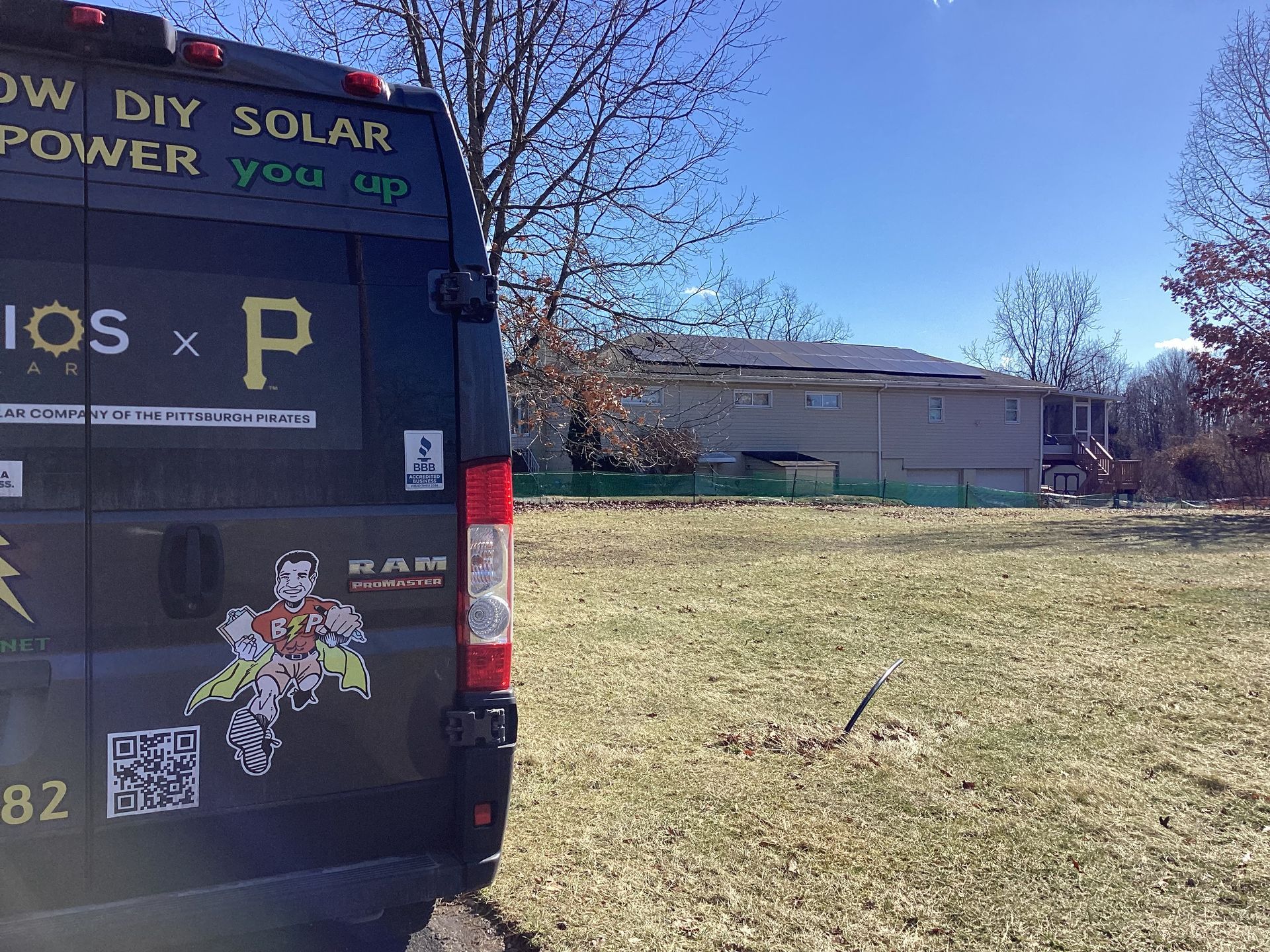 Black van with solar power graphics parked on grassy field, house in background.