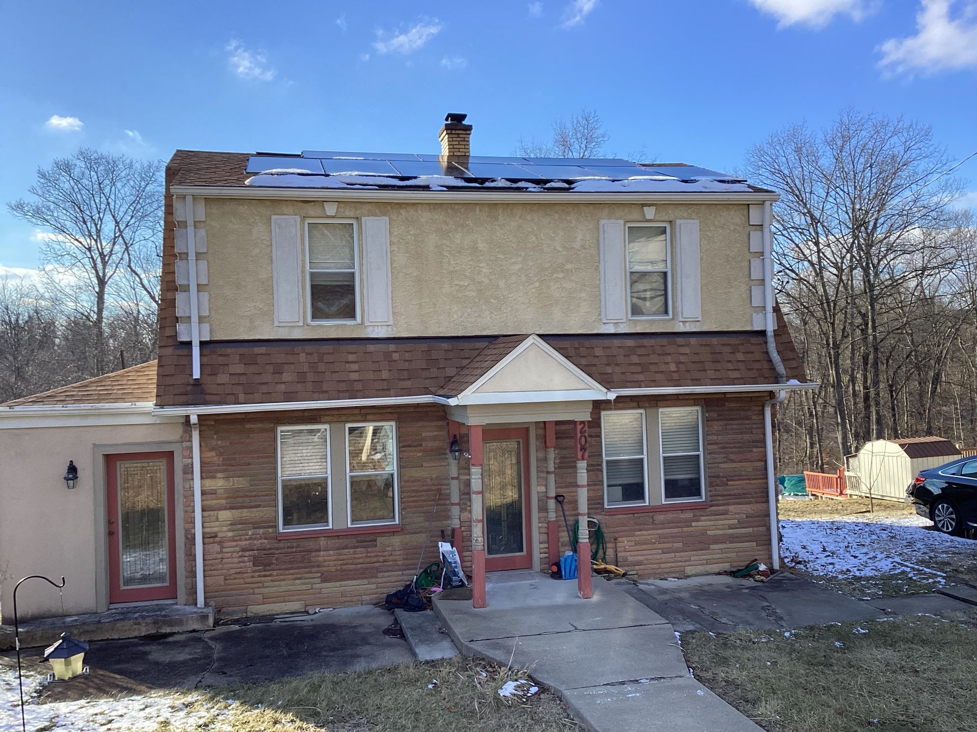 Two-story house with brick and tan stucco exterior, porch, and a patch of snow on the roof.